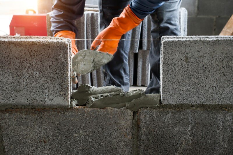 Foto de um pedreiro fazendo um muro de blocos com cimento | Como é a alvenaria de um prédio em construção | Guia da Tenda | Blog da Tenda