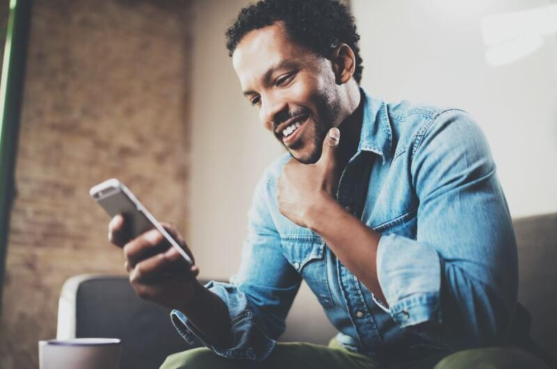Aplicativos para ajudar a manter a rotina de limpeza em casa | Foto de um homem sorrindo enquanto olha o celular | Casa e Decoração | Blog da Tenda