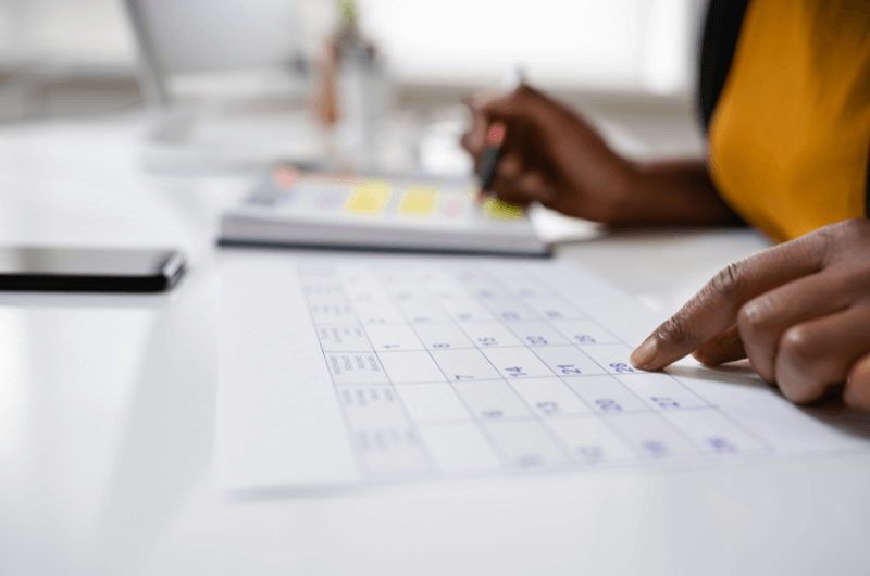 Cronograma de limpeza diária para imprimir | Foto de uma pessoa olhando um calendário e fazendo anotações em um caderno | Casa e Decoração | Blog da Tenda