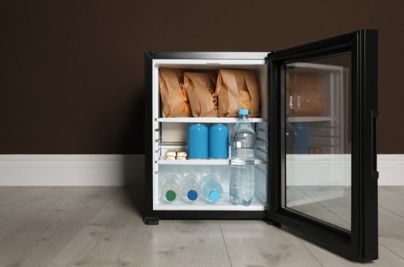 Frigobar | Foto de um frigobar na cor preta, com a porta aberta e algumas bebidas e alimentos na parte de dentro | Tenda explica | Blog da Tenda