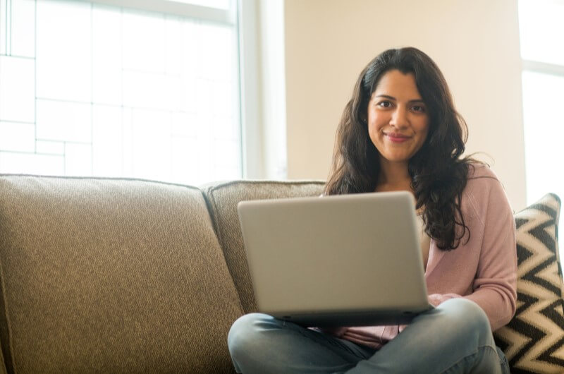 Mulher sentada sorrindo com computador na mão | O que é o Minha Casa Minha Vida | Guia da Tenda || Blog da Tenda