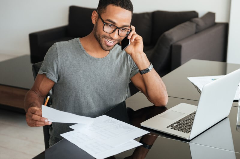 Foto de um homem negro com documentos nas mãos e ligando no celular | Quais documentos para comprovar renda em um financiamento | Guia da Tenda | Blog da Tenda