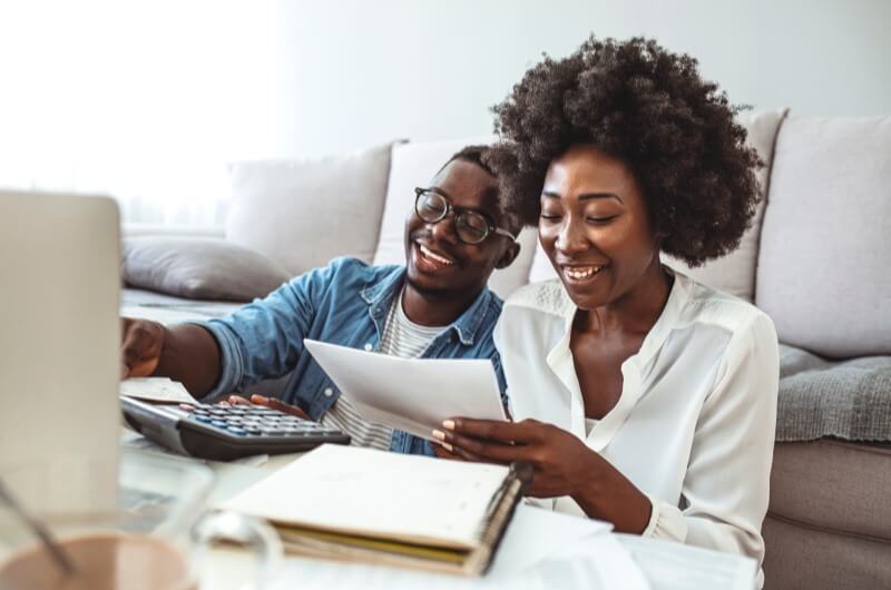 Financiamento Casa Verde e Amarela | Foto de um casal sorrindo calculando e pesquisando na internet | Guia da Tenda | Blog da Tenda