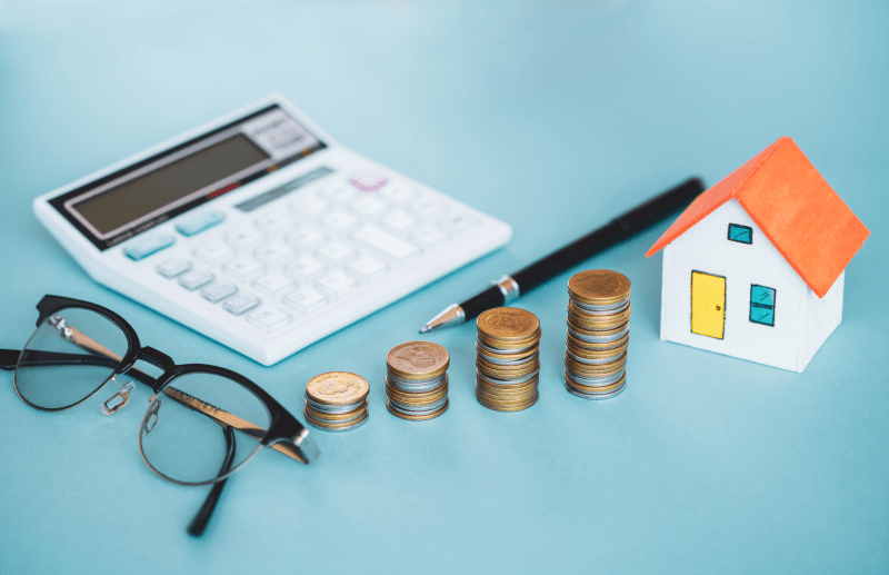 Foto de uma calculadora, óculos, moedas, caneta e uma casinha | Como é feito o cálculo da taxa condominial | Blog da Tenda