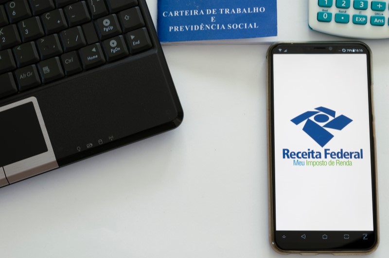 Como declarar imposto de renda autônomo | Foto de um celular com o programa da Receita Federal, notebook, carteira de trabalho e calculadora | Eu Dou Conta | Blog da Tenda
