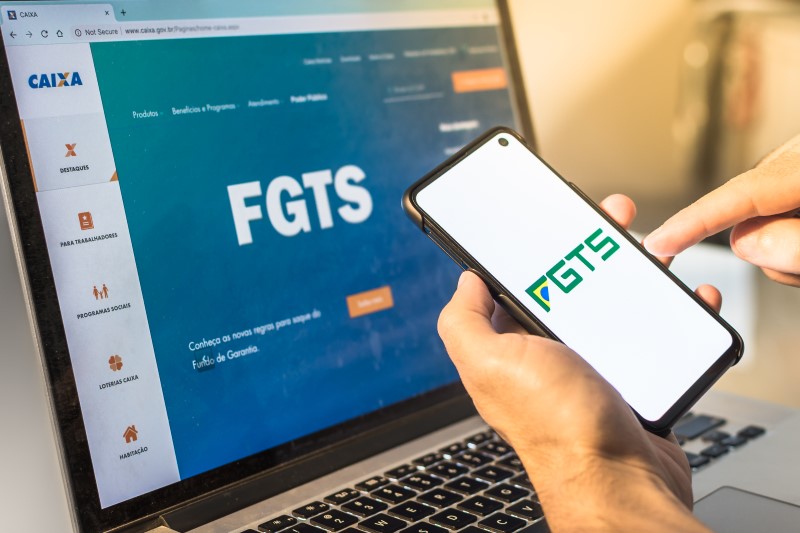 Como utilizar o FGTS como valor de entrada do seu financiamento | Foto de uma pessoa segurando celular com a logo do FGTS na tela e no computador | Guia da Tenda | Blog da Tenda