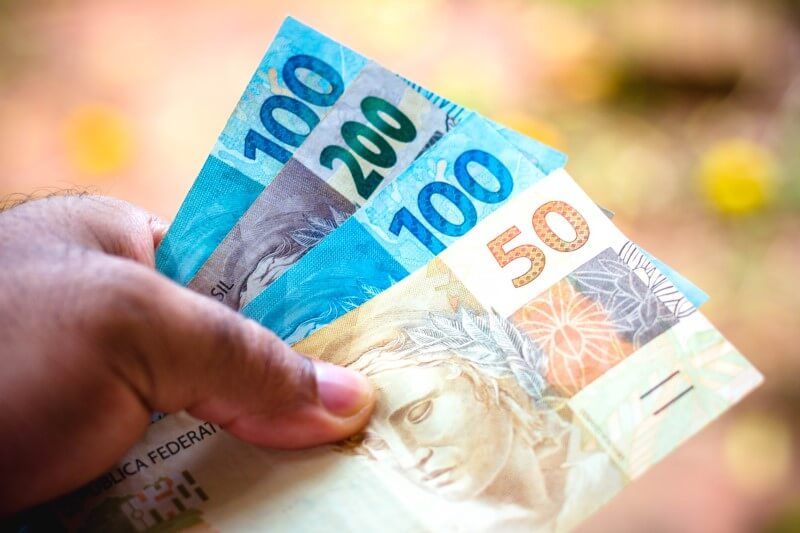 Foto de mão segurando notas de dinheiro | Como pagar o Imposto Predial | Blog da Tenda 