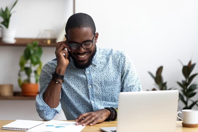 Foto de homem negro sorrindo no celular e vendo papeis e notebook | Declaração de imóvel de herança | Blog da Tenda