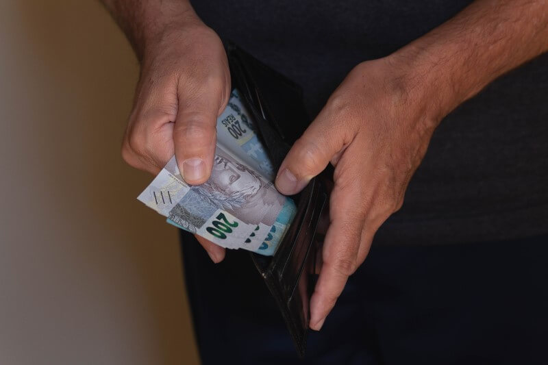 Mãos de homem pegando dinheiro na carteira | Como diminuir valor de financiamento | Blog da Tenda