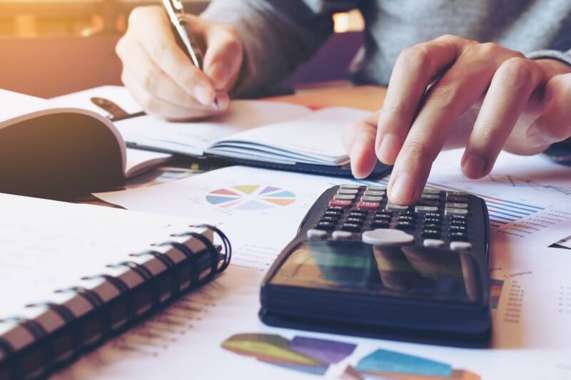 Mãos de homem com calculadora, papéis e caderno | Como diminuir o valor do financiamento de imóveis | Blog da Tenda
