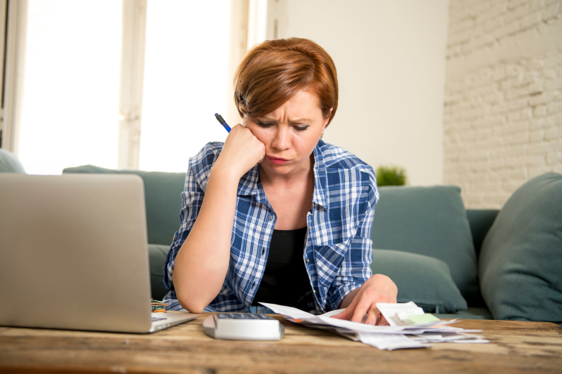 Foto de mulher preocupada fazendo as contas das dívidas na calculadora | Como financiar um apartamento com salário mínimo | Guia da Tenda | Blog da Tenda