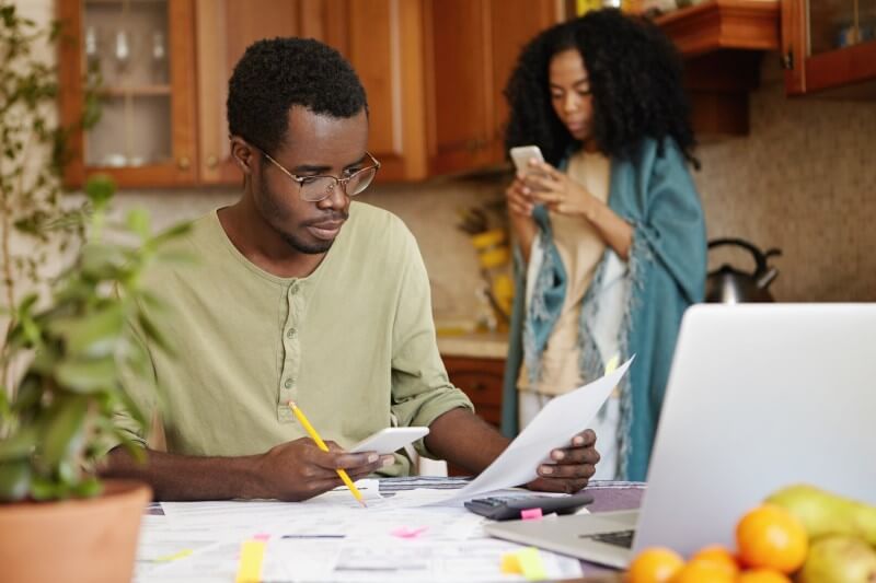 Foto de uma casal negro fazendo as contas no celular e no notebook | Como pagar as contas | Economize | Blog da Tenda