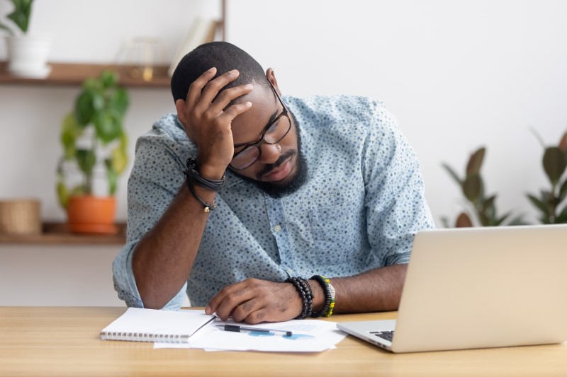 Foto de homem negro preocupado com dívidas olhando para o computador | Organizando as finanças | Economize | Blog da Tenda