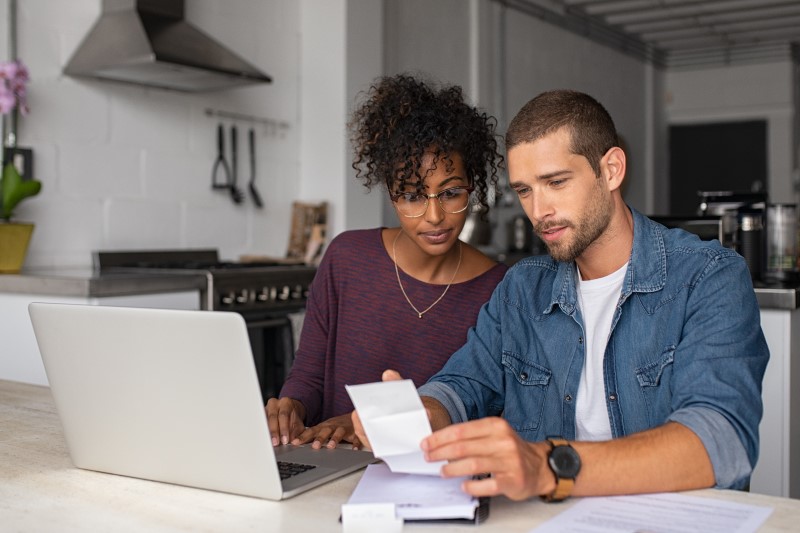Foto de um casal conferindo as contas no computador | Como pagar as dívidas | Economize | Blog da Tenda