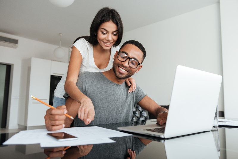 Foto de um casal organizando as finanças com computador | Comprar apartamento com salário mínimo | Guia da Tenda | Blog da Tenda