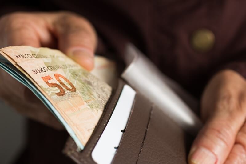 Foto de uma pessoa pegando dinheiro na carteira | Como pagar as contas: pague à vista | Economize | Blog da Tenda