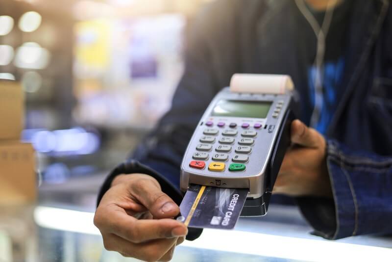 Foto de uma pessoa pagando com cartão de crédito na maquininha | Como pagar as dívidas | Economize | Blog da Tenda