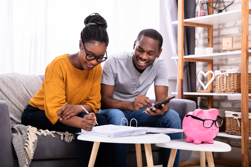 Foto de um casal jovem negro fazendo as contas para poupar | Como comprar um imóvel com salário mínimo | Guia da Tenda | Blog da Tenda