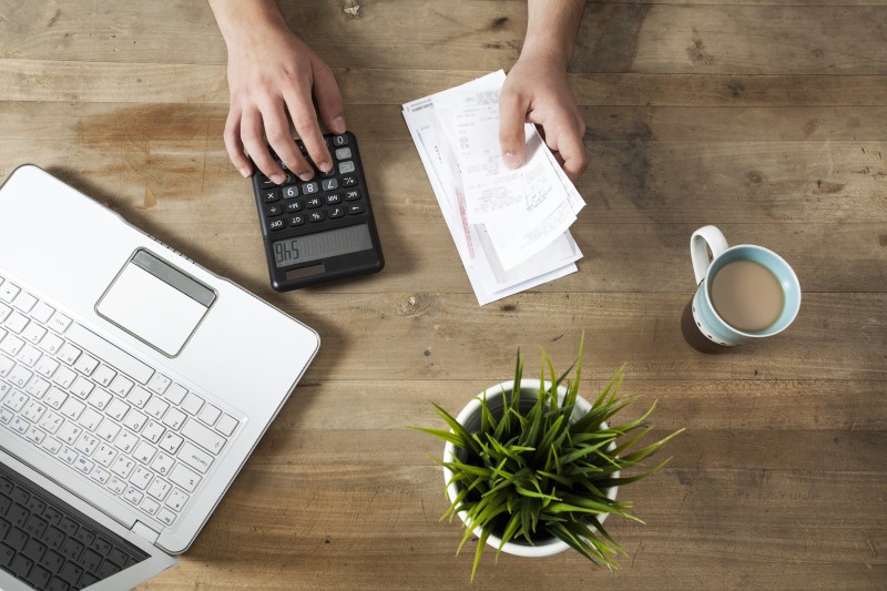 Foto de pessoa calculando notas fiscais na calculadora e computador | Organização Financeira | Economize | Blog da Tenda