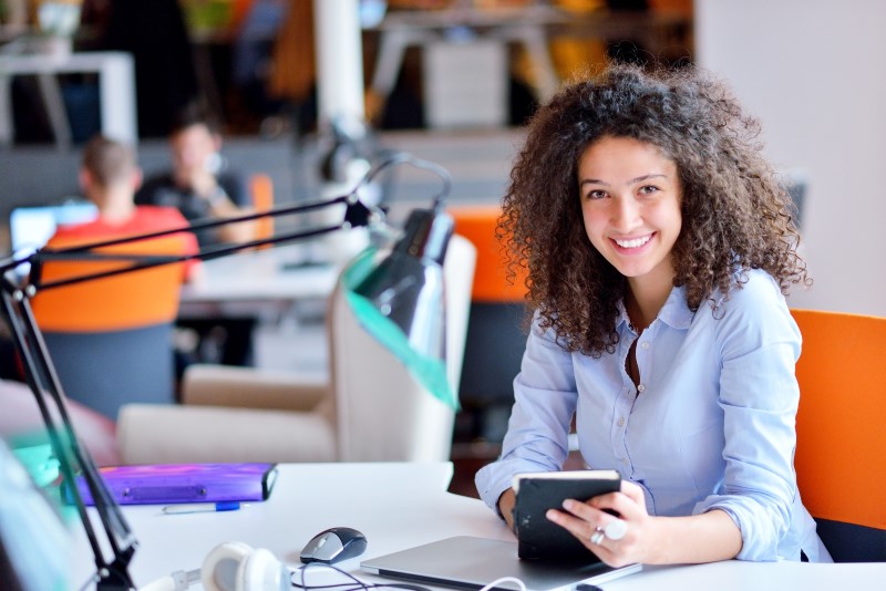 Foto de uma moça morena sorrindo na mesa de trabalho | Como ter independência financeira | Guia da Tenda | Blog da Tenda