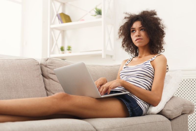 Foto de uma mulher negra sentada no sofá pesquisando na internet com dúvida | Como comprar um apartamento ainda jovem | Guia da Tenda | Blog da Tenda