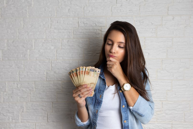 Foto de uma mulher segurando dinheiro com dúvida | Posso financiar um imóvel com salário mínimo | Guia da Tenda | Blog da Tenda
