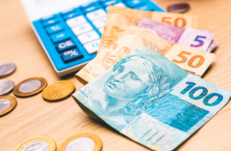 Foto de cédulas de dinheiro, moedas e uma calculadora | Quais são as taxas de juros do Casa Verde e Amarela | Minha Casa Minha Vida | Blog da Tenda