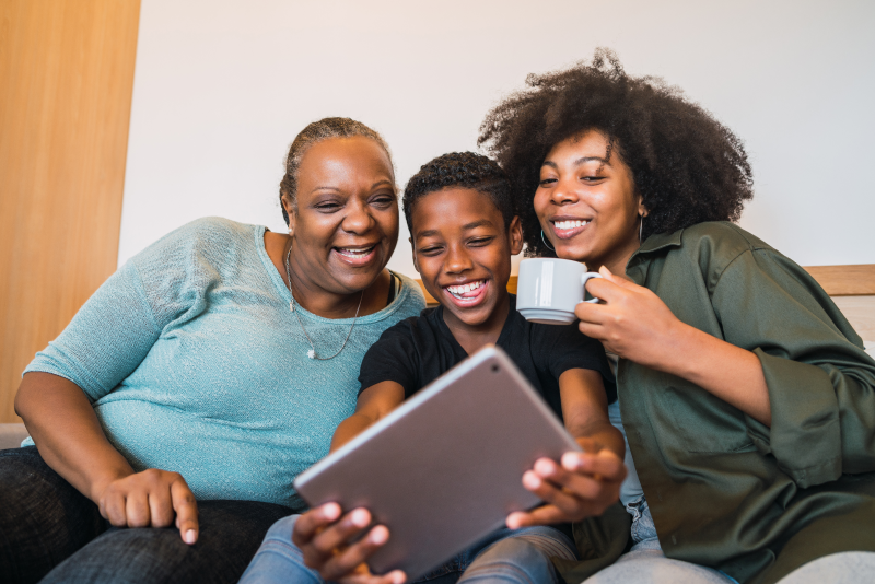 Foto de uma avó com netos olhando o tablet | Casa Verde e Amarela prioriza famílias chefiadas por mulheres e com idosos, crianças e adolescentes | Minha Casa Minha Vida | Blog da Tenda 