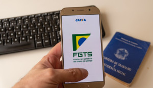 Foto de um celular com logo do FGTS, uma carteira de trabalho e um teclado de computador | Como usar o FGTS no Casa Verde e Amarela | Minha Casa Minha Vida | Blog da Tenda