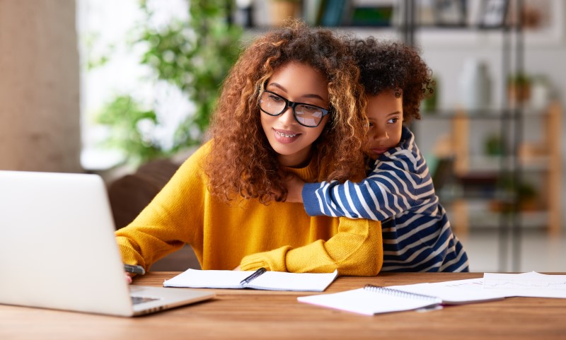 Foto de uma mulher trabalhando em casa com o filho | Benefícios do Casa Verde e Amarela para mulheres chefes da família | Minha Casa Minha Vida | Blog da Tenda 