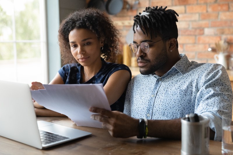 Como financiar um imóvel | Foto com um casal de negros analisando papéis na frente do computador | Guia da Tenda | Blog da Tenda