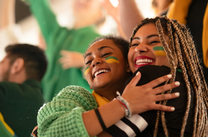 Qual vai ser o primeiro jogo do Brasil na Copa de 2022 | Foto de duas amigas torcendo pelo Brasil | Minha Casa Minha Vida | Blog da Tenda