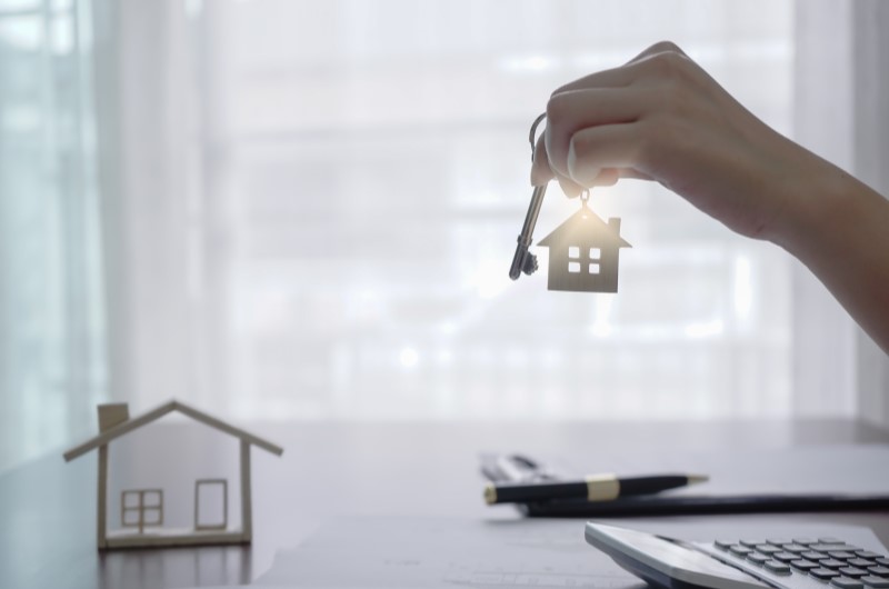 6 motivos para sair do aluguel | Foto de uma pessoa segurando as chavés da casa própria, com um casinha em miniatura ao lado | Trilha da Conquista | Blog da Tenda
