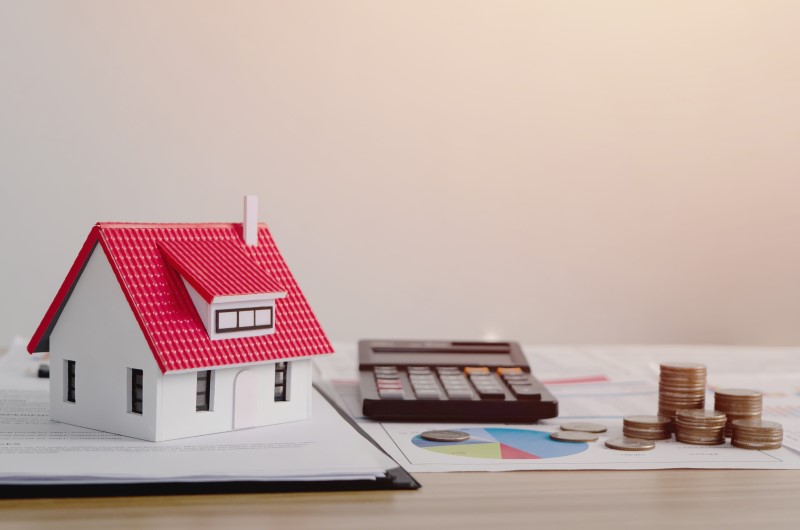 O que é amortização de financiamento | Foto de uma miniatura de casa, com uma calculadora e moedas | Trilha da Conquista | Blog da Tenda
