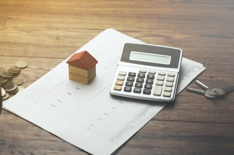 Baixas taxas de juros | Foto de uma calculadora e miniatura de casinha sobre um papel | Minha Casa Minha Vida | Blog da Tenda