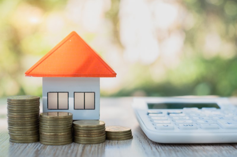 Como comprovar renda mista para financiamento imobiliário? | Foto de uma casinha com moedas e uma calculadora ao lado | Trilha da Conquista | Blog da Tenda 