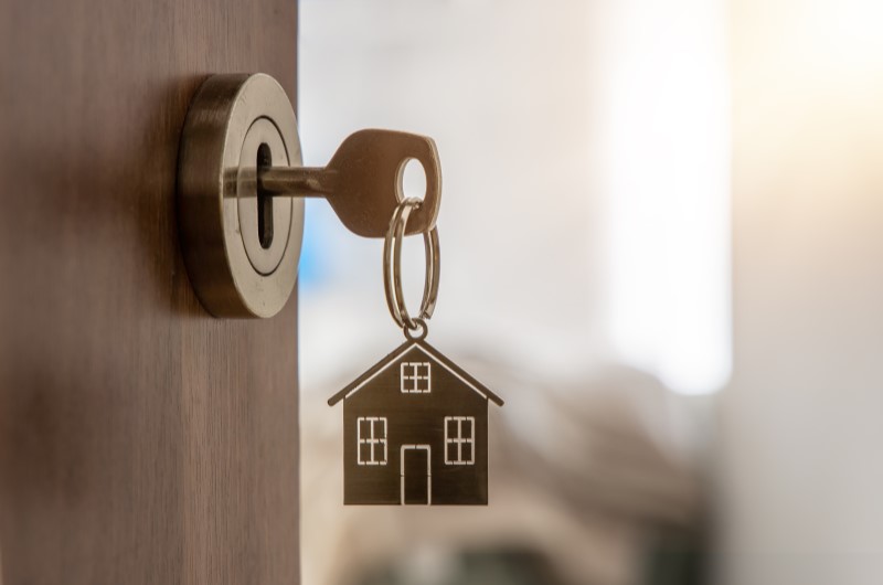 O que é o programa Mais Habitação - Compra Compartilhada? | Foto de chave em uma porta entreaberta, com um chaveiro de casinha | Trilha da Conquista | Blog da Tenda