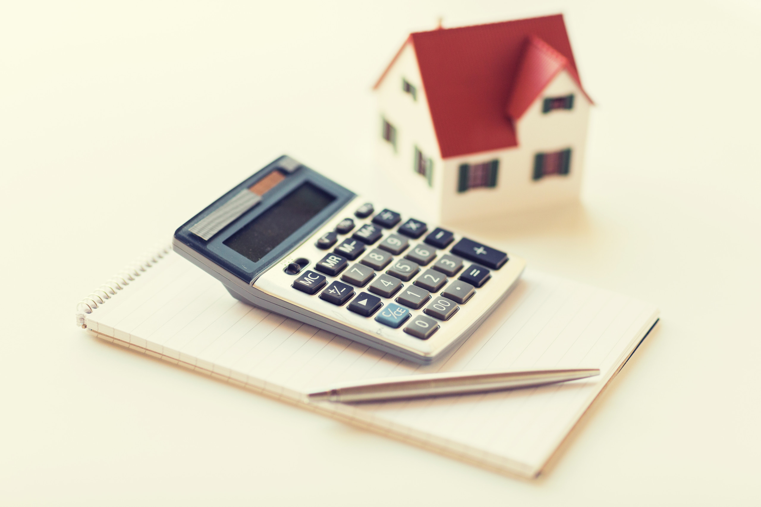 Como funciona o saldo devedor no financiamento imobiliário? | Foto de uma casinha com um caderno, caneta e calculadora | Trilha da Conquista | Blog da Tenda
