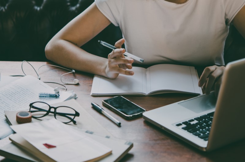 Como ter a análise de crédito aprovada? | Foto de uma pessoa usando o notebook, com um celular, óculos e caderno sobre a mesa | Dúvidas sobre dívidas | Eu Dou Conta 