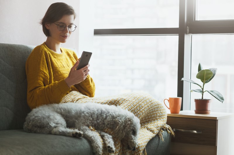 Antes de tudo: conheça alguns tipos de divisória | Foto de uma mulher sentada no sofá com um cachorro, enquanto usa o celular | Casa e Decoração | Blog da Tenda