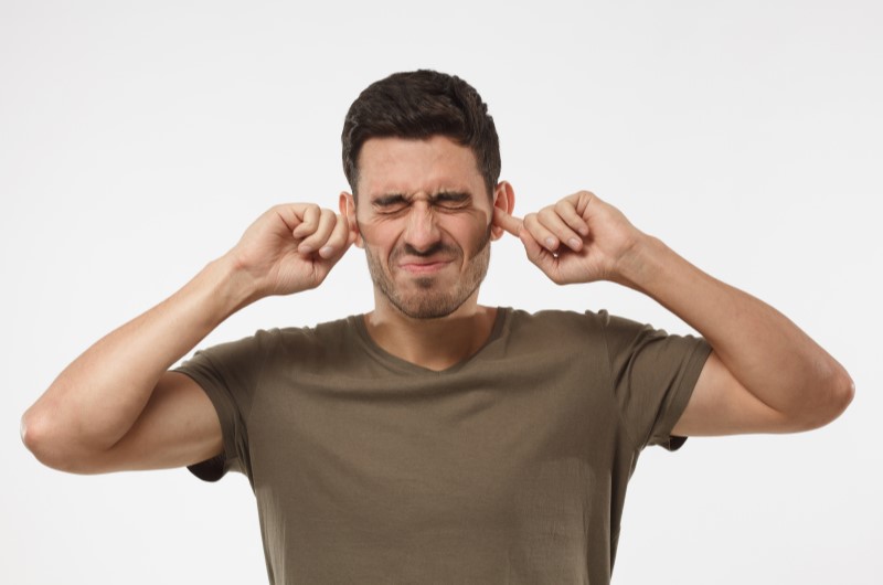 Barulho em condomínio: como mediar conflitos? | Foto de um homem com a expressão irritada, tampando os ouvidos | Viver em Condomínio | Blog da Tenda 