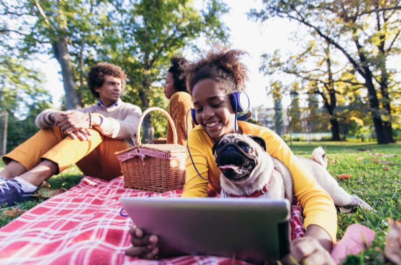 Faça um piquenique ao ar livre | Foto de uma família e seu cachorrinho fazendo um piquenique no parque | Viver em condomínio | Blog da Tenda 
