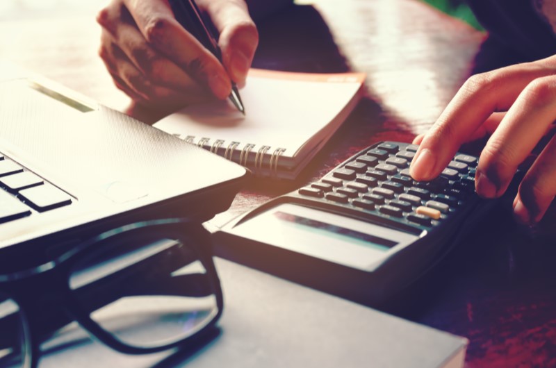 O que é a taxa de juros de um financiamento? | Foto de uma pessoa usando a calculadora e escrevendo em um caderninho | Minha Casa Minha Vida | Blog da Tenda 