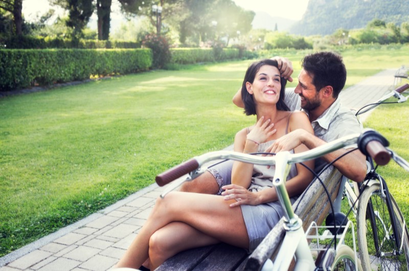 Prefira roupas leves | Foto de um casal com uma bicicleta, sentados em um banco no parque | Viver em condomínio | Blog da Tenda 