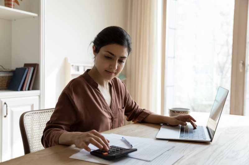 Como calcular o dissídio salarial? | Foto de uma mulher usando o notebook e calculadora ao mesmo tempo | Trilha da Conquista | Blog da Tenda