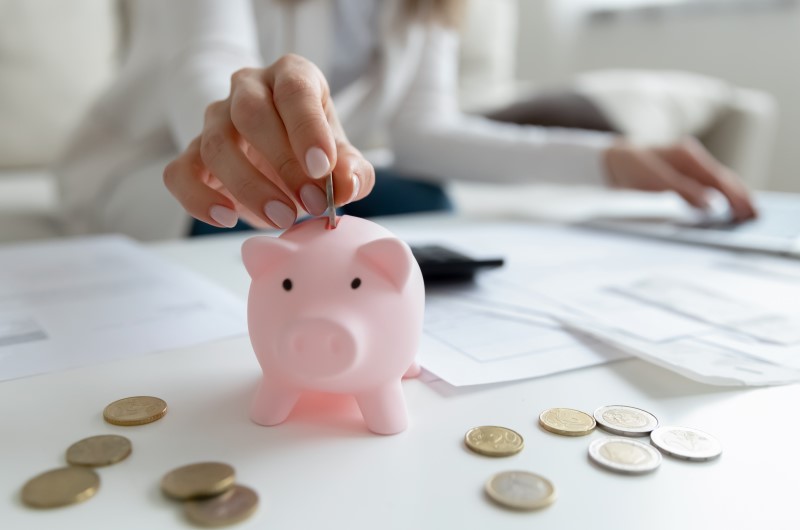 Faça a sua poupança render | Foto de uma pessoa colocando moedas em um cofrinho | Economia e renda extra | Eu Dou Conta