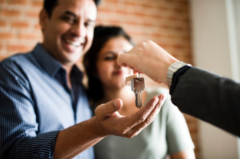 Mais Habitação - Compra Compartilhada | Foto de uma pessoa entregando a chave da casa própria para um casal | Trilha da Conquista | Blog da Tenda