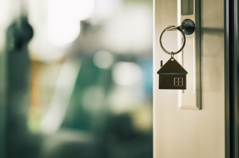 Quais são os outros benefícios do Minha Casa, Minha Vida? | Foto de um porta entreaberta com um chaveiro de casinha na fechadura | Trilha da Conquista | Blog da Tenda
