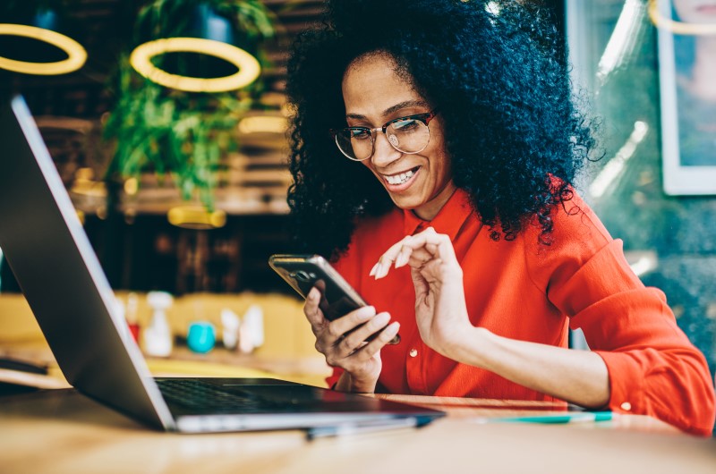 Custo-benefício | Foto de uma moça sorridente pesquisando no celular | Casa e decoração | Blog da Tenda