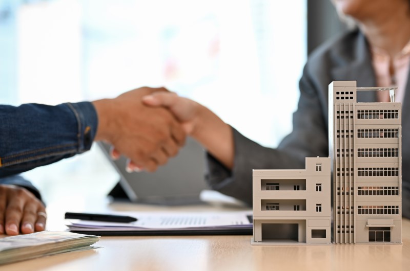 Principais características do SFI? | Foto de uma miniatura de prédio, com duas pessoas apertando as mãos ao fundo | Trilha da Conquista | Blog da Tenda